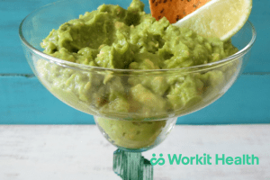 A margarita glass full of guacamole, garnished with lemon