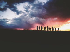 Nine people stand atop a hill, silhouetted by the rising sun