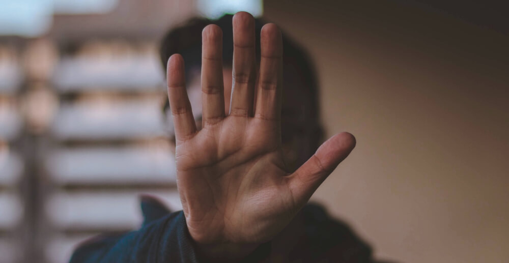 A person holding their hand up in the flat, palm-out gesture that means "stop."