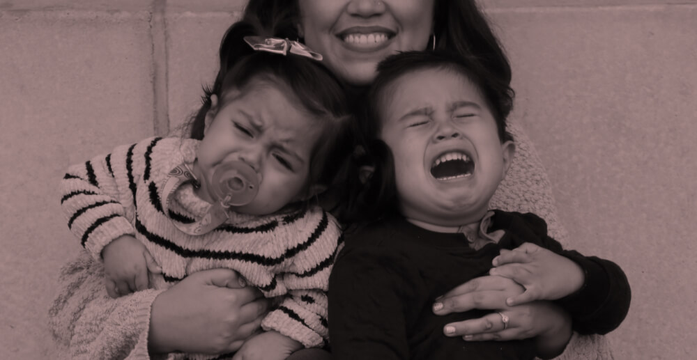 Woman holding two screaming toddlers. Confessions of an alcoholic mom