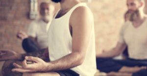 Several men in yoga clothing sit meditatively in lotus position