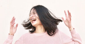 Young Asian woman laughs with her hands in the air and her hair swinging around her.