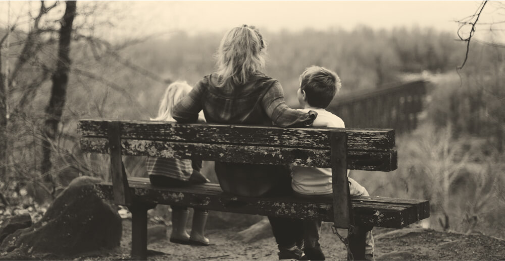 View from behind of a woman on a wooden bench with a child on either side of her. Confessions of an alcoholic mom, part 2