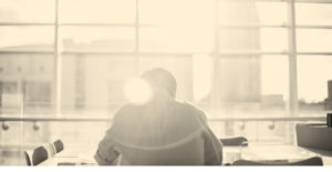 Man in an office, with a glare of light obscuring his outline. Opioid addiction at work.