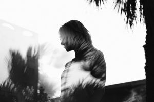 a double exposure image of palm tree shadows over the silhouette of a woman. The image is black and white.
