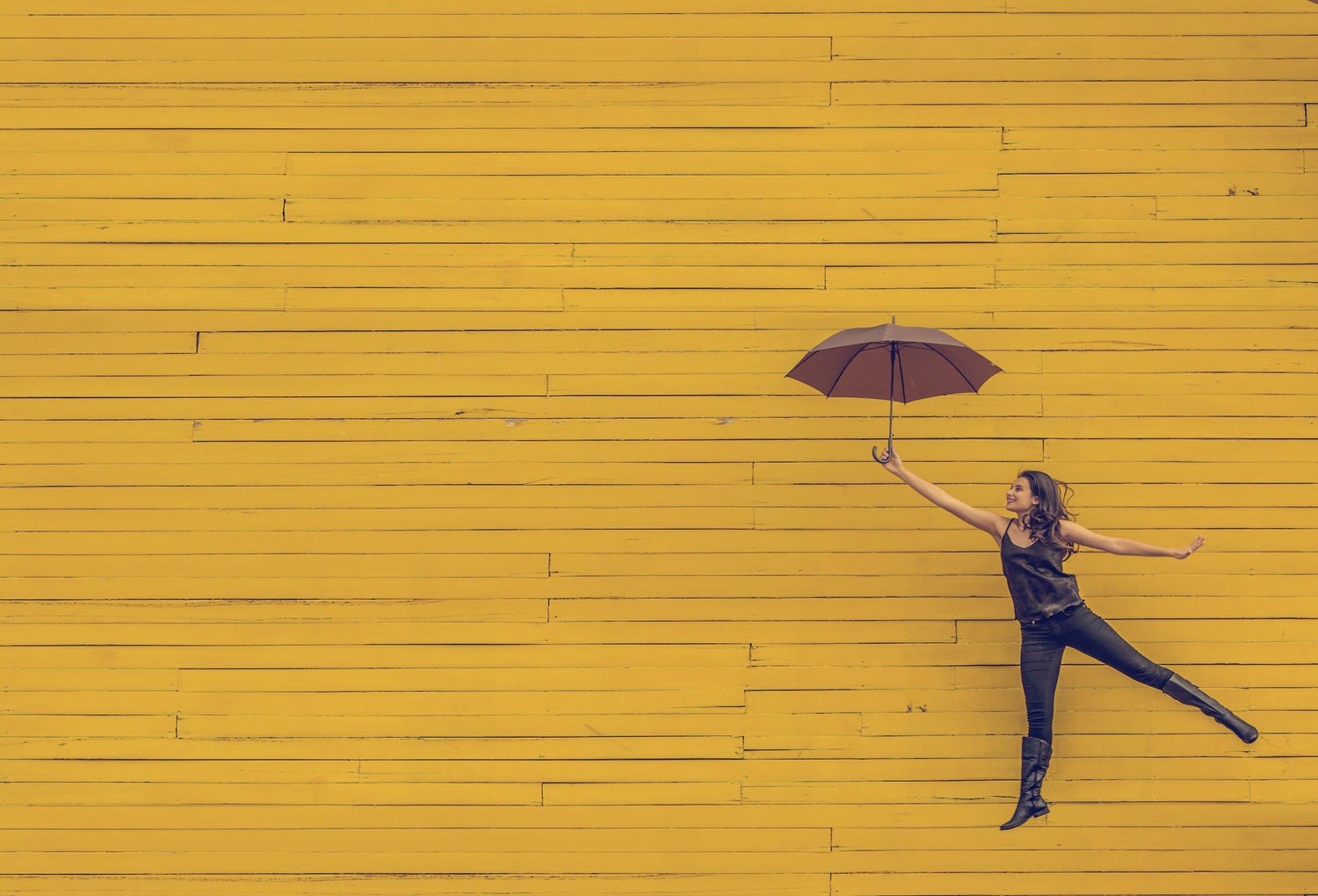 woman-jumping-with-umbrella-yellow-wall