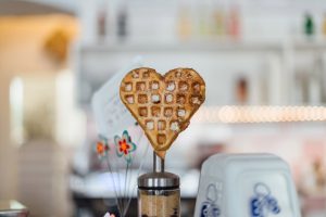 A heart-shaped waffle stands upright on a stick in a cheerful kitchen.