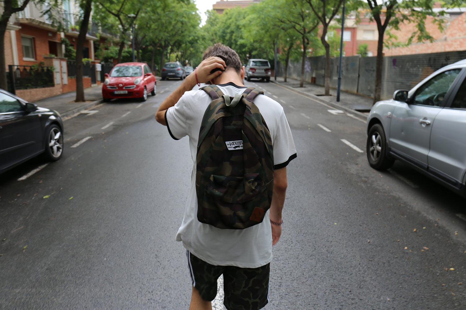 View from behind of a man with a backpack walking down the street, his posture looking discouraged.