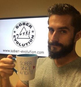 Austin Cooper of Sober Evolution holds a coffee mug that reads "Sober since 4/10/13"