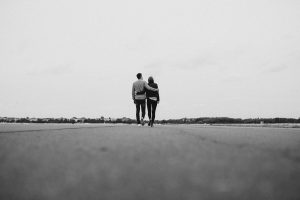 Black and white photo of a man and woman walking down an empty road with their arms around on another