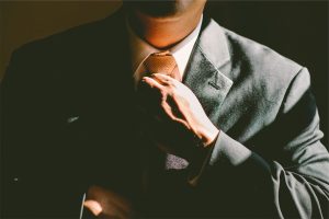 A man in a gray suit adjusts his tie