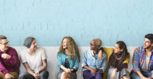 A row of people sit against a cinderblock wall, smiling and laughing together.