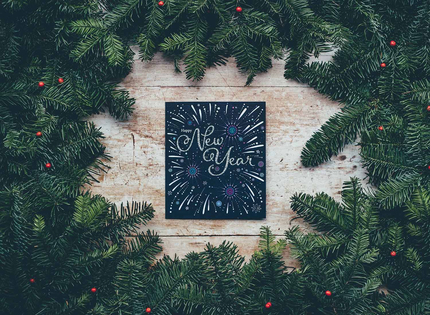 A hand-lettered sign reading "New Year" is surrounded by pine branches. Practical New Year's resolutions