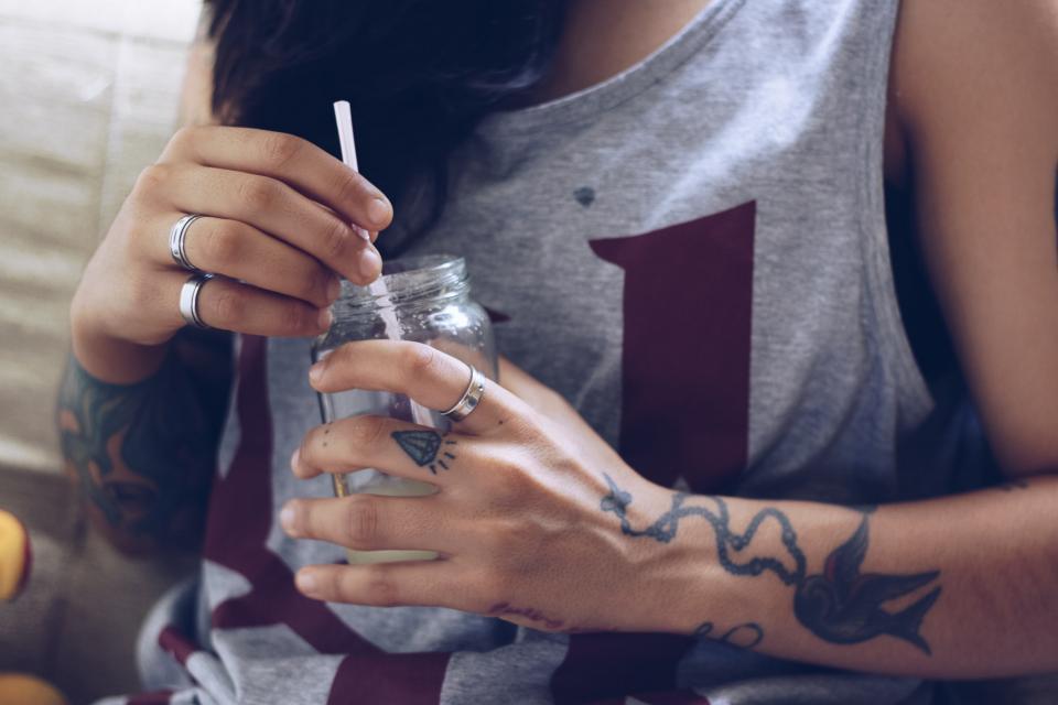 A woman with tattoos holds a drink in a mason jar. Pain Med Recovery