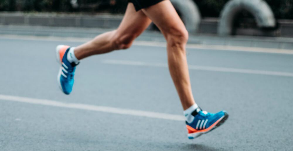Legs of a person wearing shorts and sneakers running on a street. Recovery is a marathon