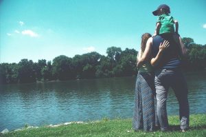 Two parents hold thier child on the shore of a lake. Be a better parent in recovery.