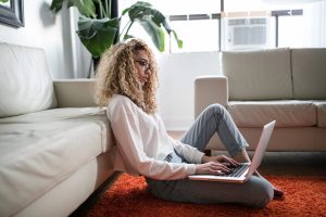 A woman sits on the floor with her laptop. Online addiction courses.