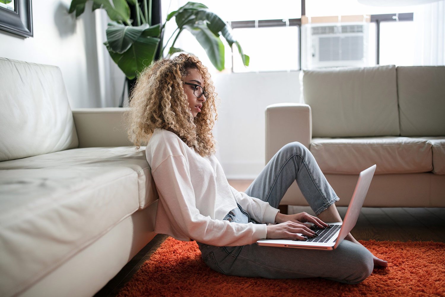 A woman sits on the floor with her laptop. Online addiction courses.