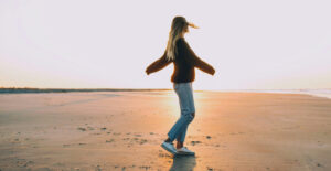 A woman in a sweater and jeans spins on the empty sands of a beach