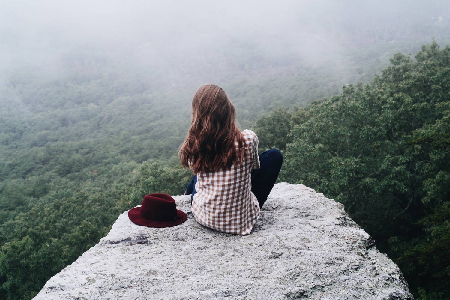 Photo of a woman sitting on a mountain looking at the view below