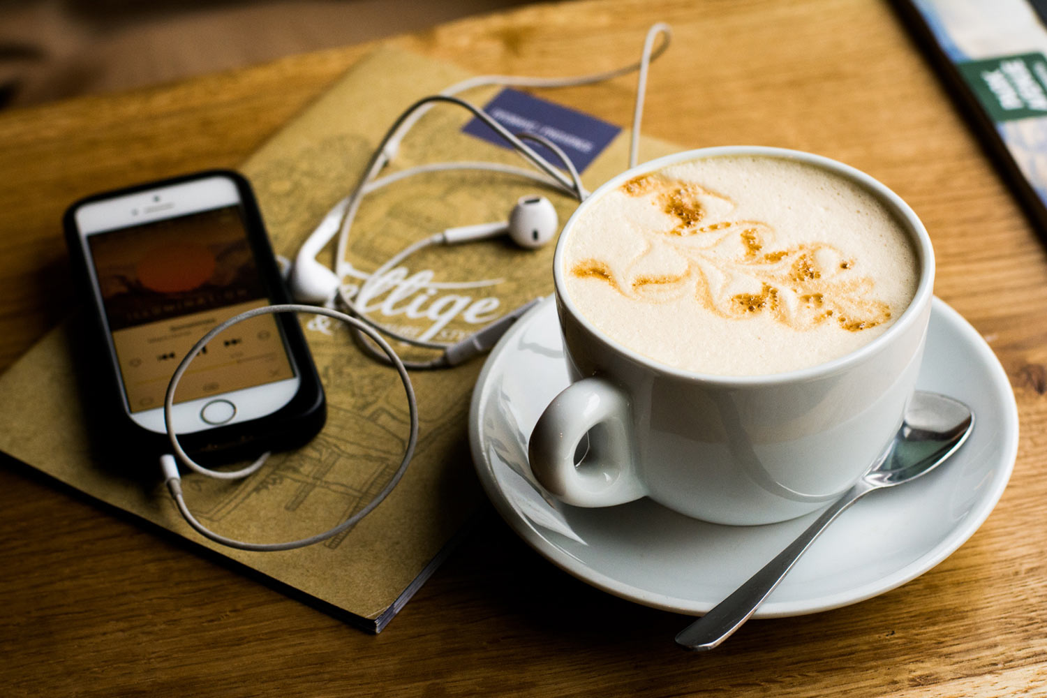A latte next to an iPhone with earbuds. Recovery podcasts