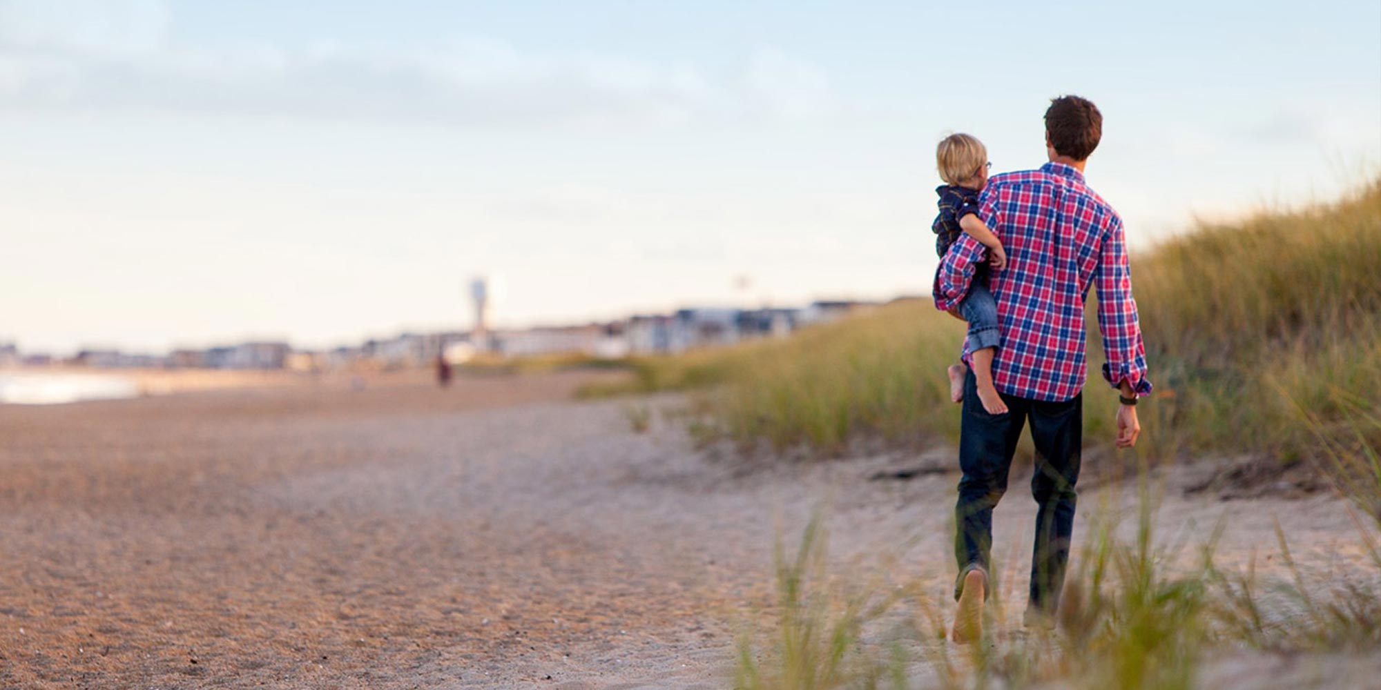 A man on the beach holding a small child on his hip