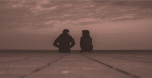 View from behind of two people sitting on the end or a pier, talking. Stay sober through a breakup