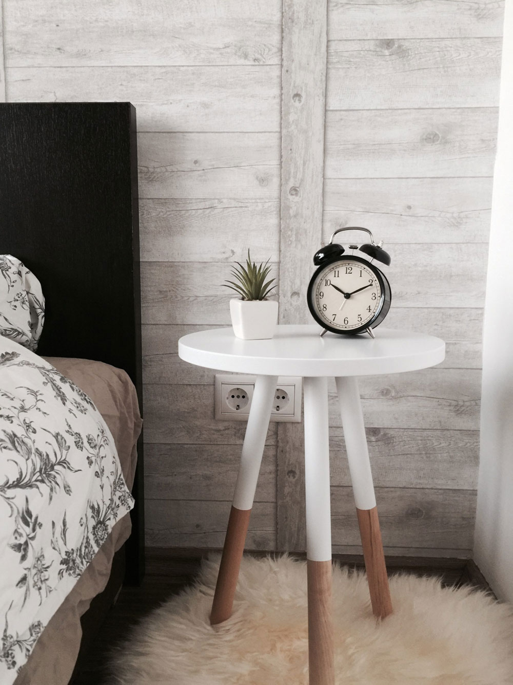 An old fashioned alarm clock on a bedside table beside a potted succulent