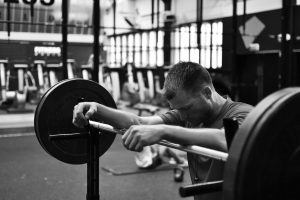 In a gym, a man leans his arms against a barbell loaded with weights