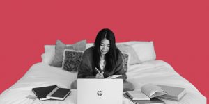 Woman sitting on the bed with a laptop and several open books around her