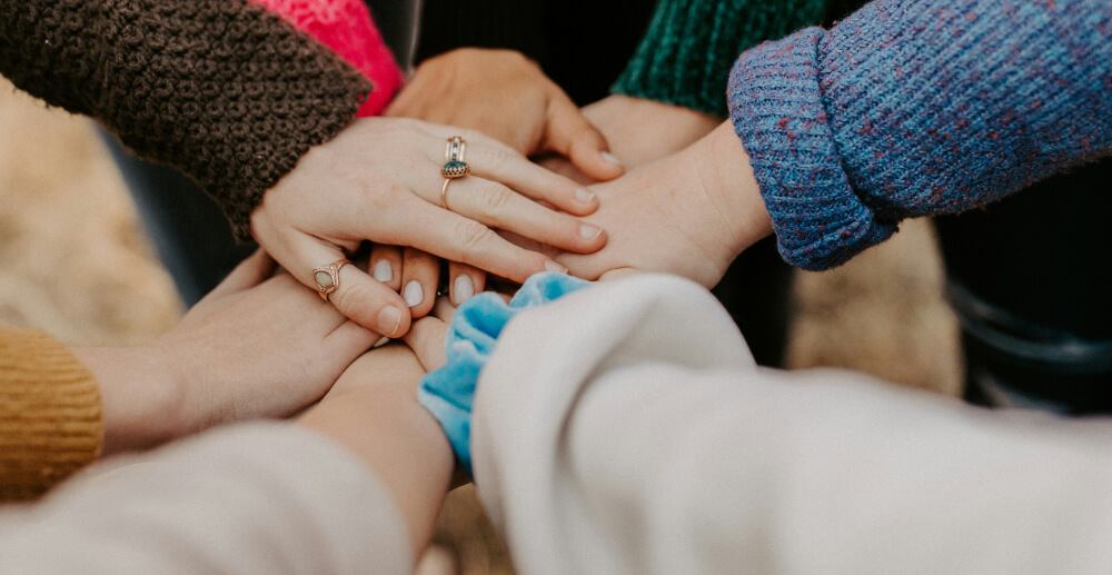 Hands in! A circle of people supporting one another with their hands stacked up.