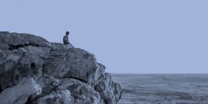 Sitting alone on a rock, looking at the ocean.