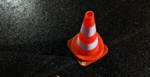 A bright orange safety cone sits on wet, shiny, black asphalt