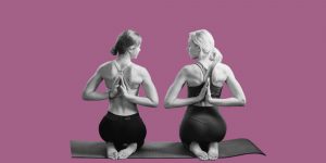 Two women kneel next to one another on mats, doing yoga