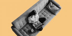 View from above of a woman on a sofa working on a laptop. Drinking while working from home