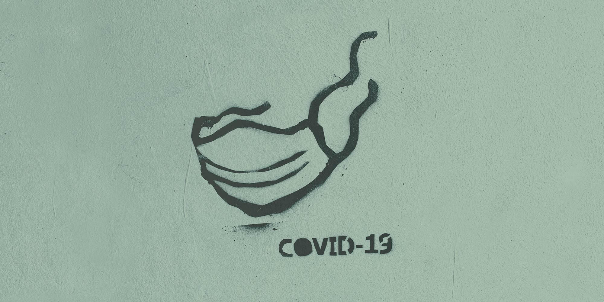 Spray painted art of a face mask and the words COVID-19. Reflecting on a year of COVID