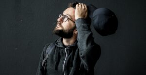 A man in a hoodie looks up questioningly, a baseball cap in his hand.
