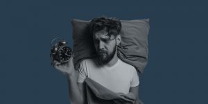 Sleepless man holding an alarm clock. Does alcohol cause insomnia?