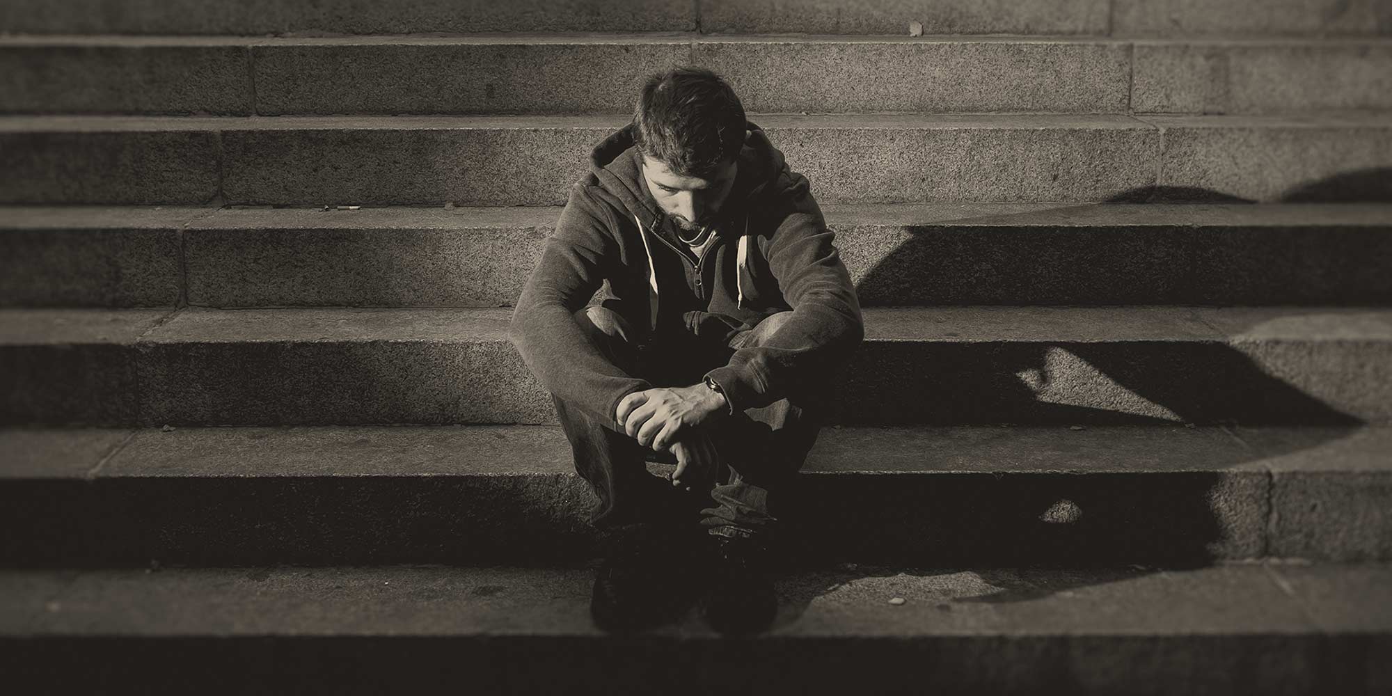 Man in a hoodie sitting sadly on outdoor stairs. Does withdrawal cause depression?