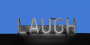 Neon sign reading "Laugh" against a blue background. Stand-up comedy in addiction recovery