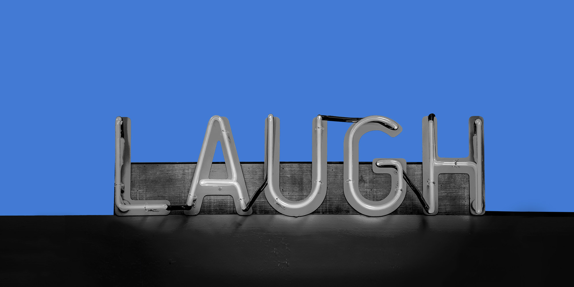 Neon sign reading "Laugh" against a blue background. Stand-up comedy in addiction recovery