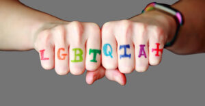 Two fists with LGBTQIA+ written across the knuckles in rainbow colors. Mental Health resources for the LGBTQIA community