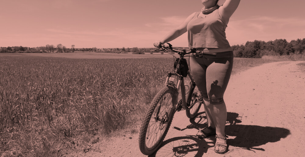 Peach overlay colors a black and white image of a woman standing next to her bicycle in a sunny field.