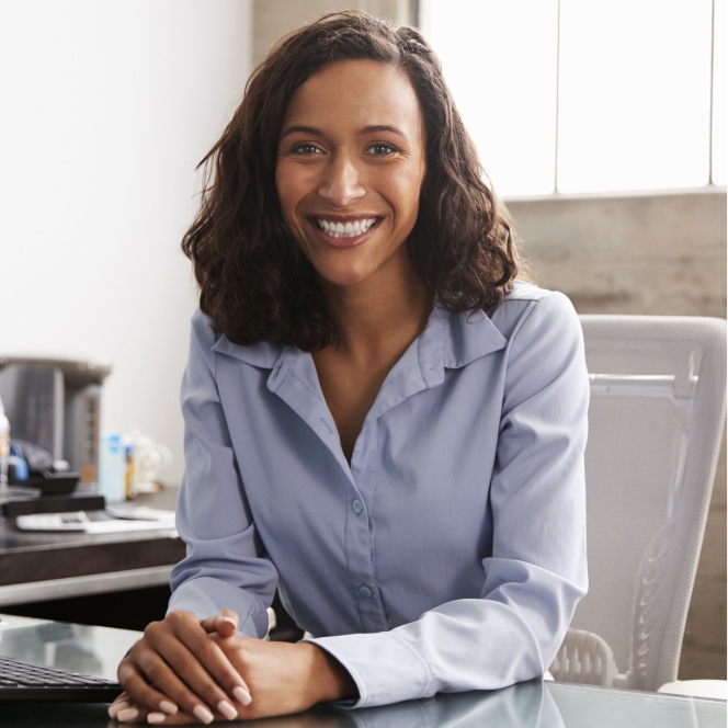 A young business women sitting at her desk hands folded and smiling