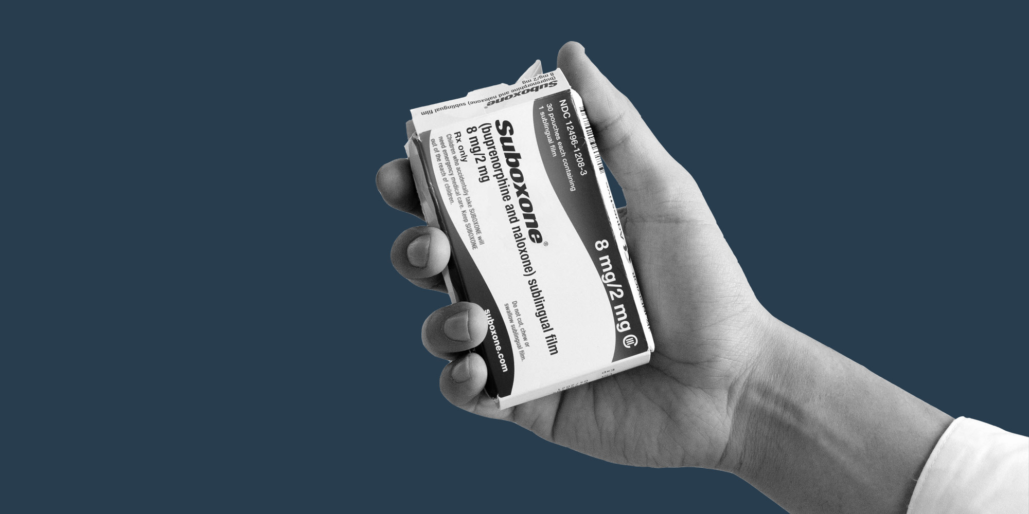 Hand holding a Suboxone box against a dark blue background