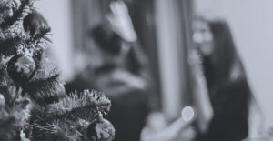 Looking past a decorated Christmas tree to where two people are talking, out of focus. Protecting your sobriety during the holidays.