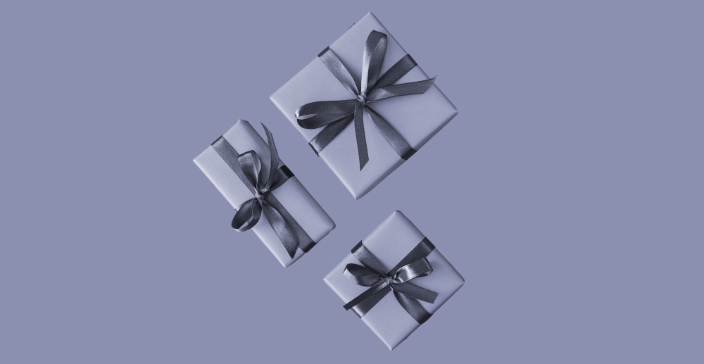 Three wrapped gifts in monochrome on a blue-gray background. Holiday gift guide for people in addiction recovery.