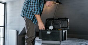 A man leans down toward an open toolbox, his hand reaching in to grab a tool.