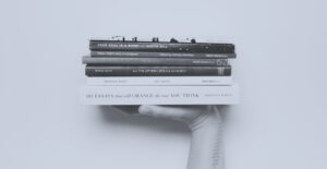 Light gray-blue color overlaying a black and white photo of a hand lifting a stack of books. Books to read in early recovery