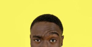 A young Black man raises an eyebrow skeptically.